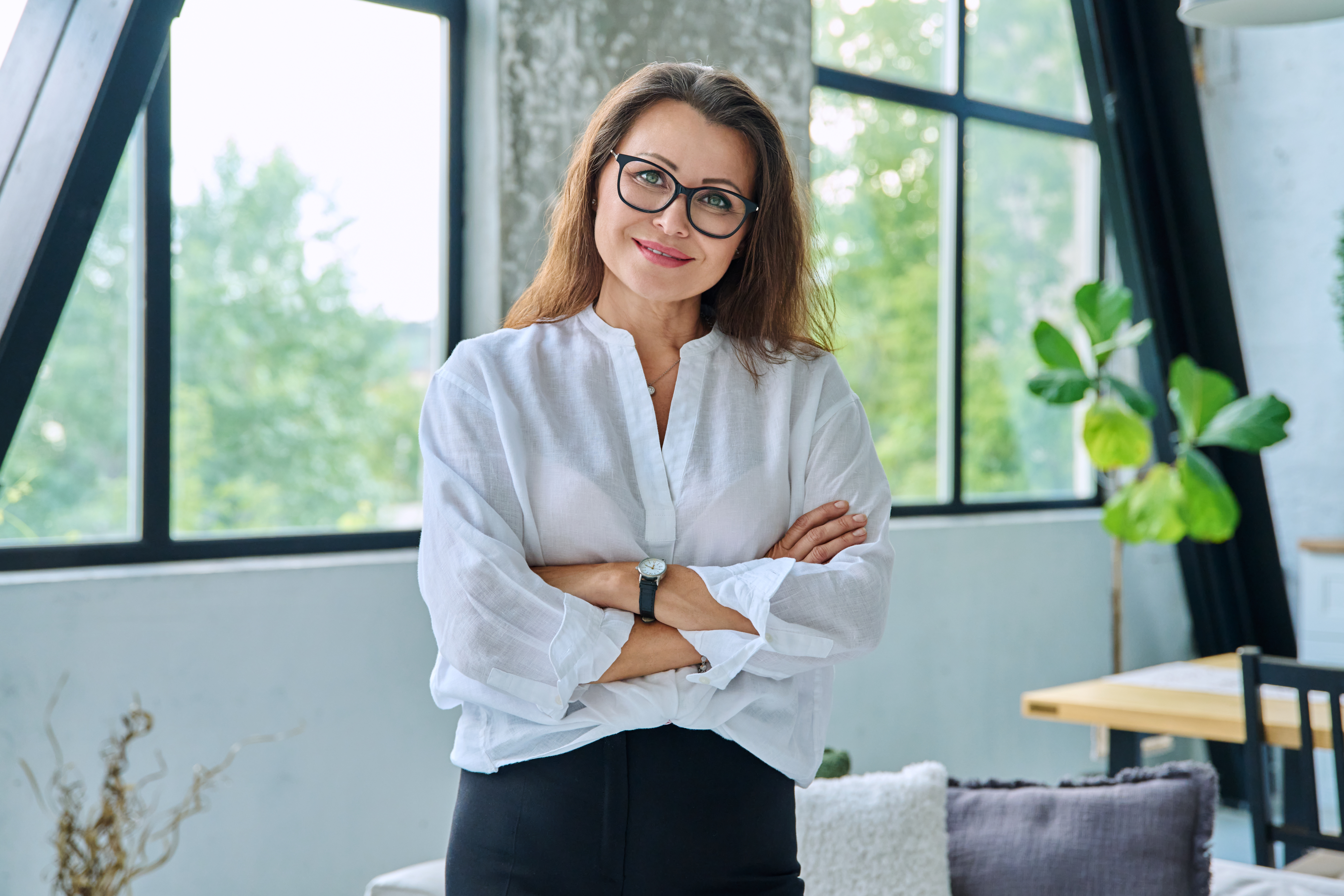 Eine junge Psychotherapeutin steht in ihrer Praxis und schaut freundlich und kompetent in die Kamera