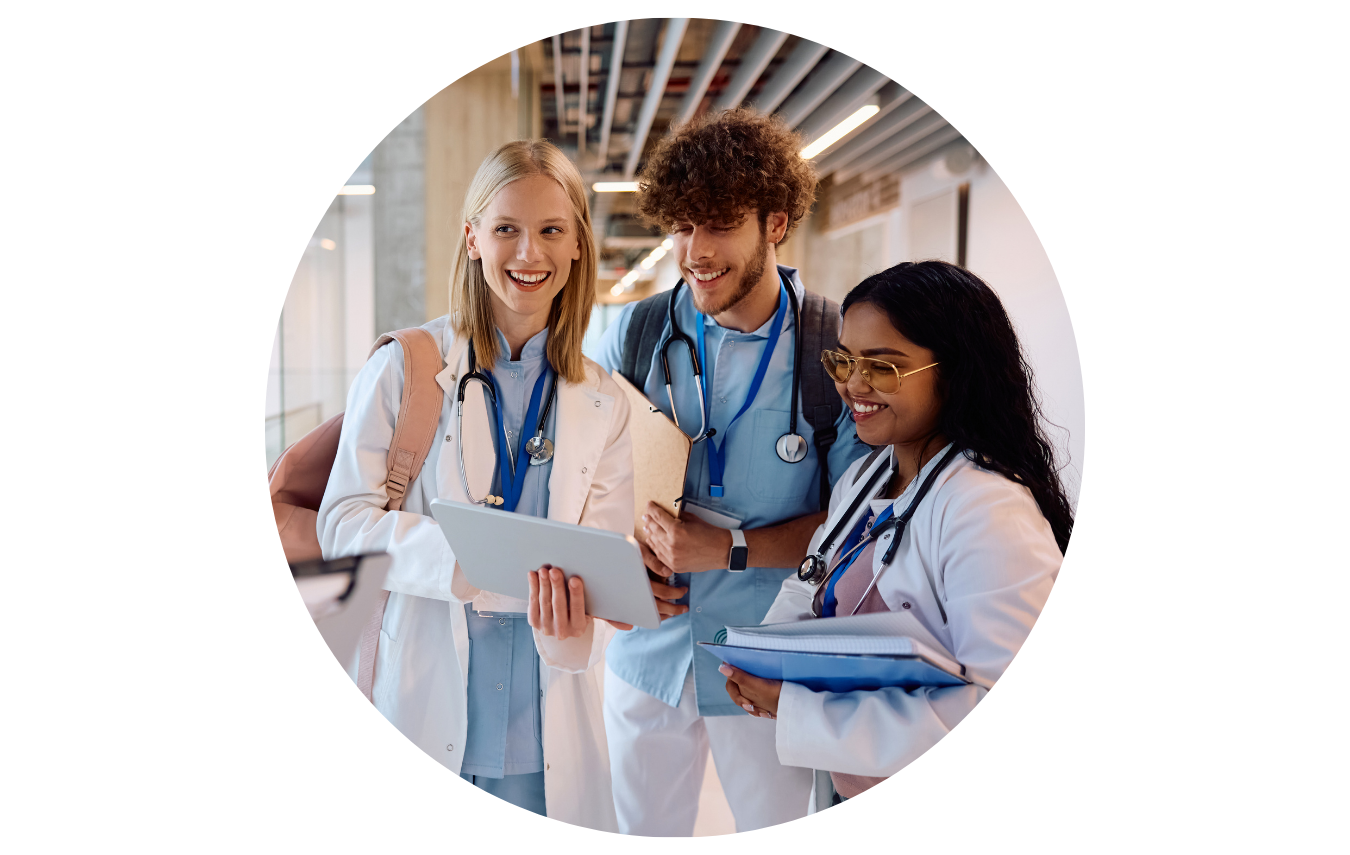 Eine Gruppe Medizinstudierende steht auf dem Gang in einer Universität und begrüßt freundlich lachend eine weitere Studentin, die auf sie zugelaufen kommt.
